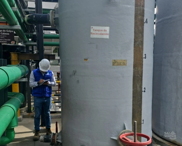 Ingeniero de SAI WATER tomando notas junto a un tanque de recirculación en PRFV con escala de nivel en metros cúbicos