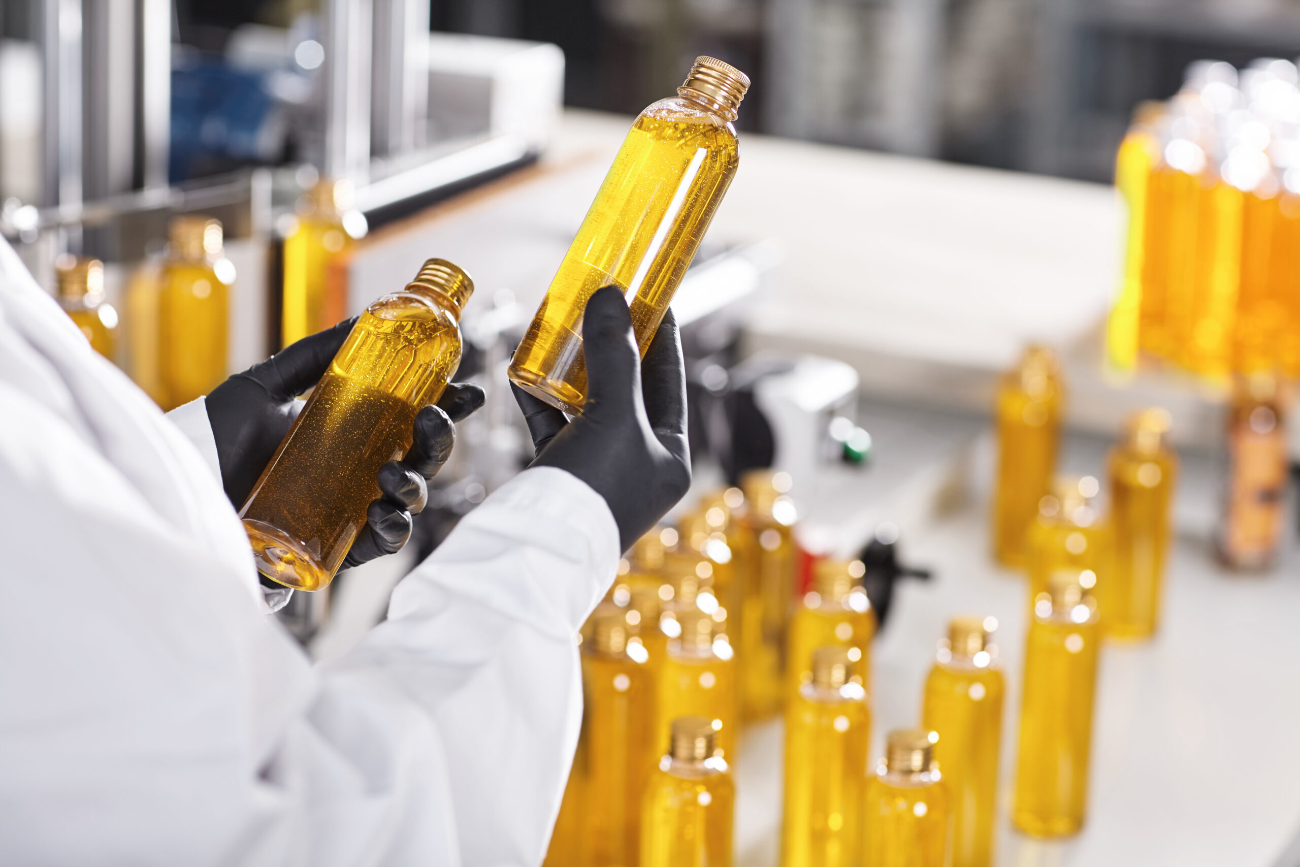 Manufacturing concept. Factory worker holding two glass bottles with yellow liquid comparing quality between them. Factory process of production shampoo. Technology, innovation and scientific concept